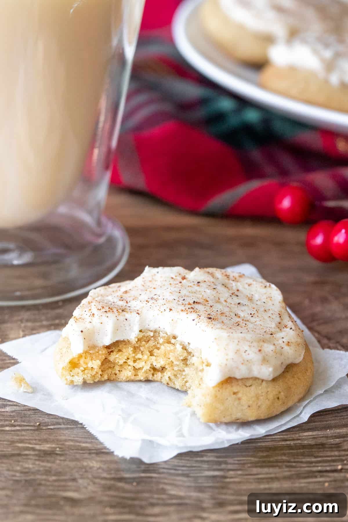 Eggnog Cookies with Creamy Eggnog Frosting — Holiday Cookie Recipe 3 Frosted eggnog cookie with a bite taken out beside a glass of eggnog