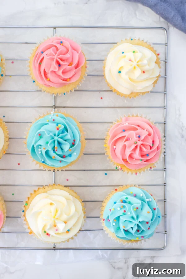 Classic Vanilla Cupcakes with Smooth Vanilla Buttercream Frosting 3 Vanilla cupcakes with vanilla frosting on a cooling rack, from overhead.