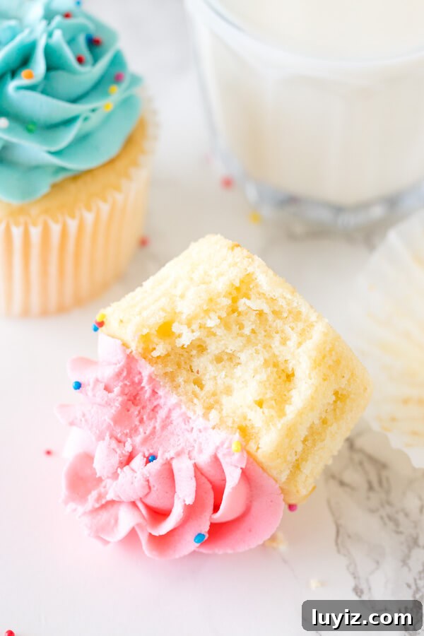 Classic Vanilla Cupcakes with Smooth Vanilla Buttercream Frosting 5 Cupcake with pink frosting with a bite taken out of it with a glass of milk.