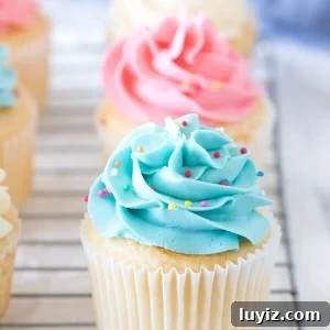 Classic Vanilla Cupcakes with Smooth Vanilla Buttercream Frosting 6 Vanilla cupcakes with colored frosting on a cooling rack.
