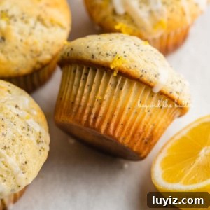 Lemon Poppy Seed Muffins with Zesty Glaze Recipe 14 Randomly placed lemon poppy seed muffins on a parchment paper-lined baking sheet with half of a lemon.