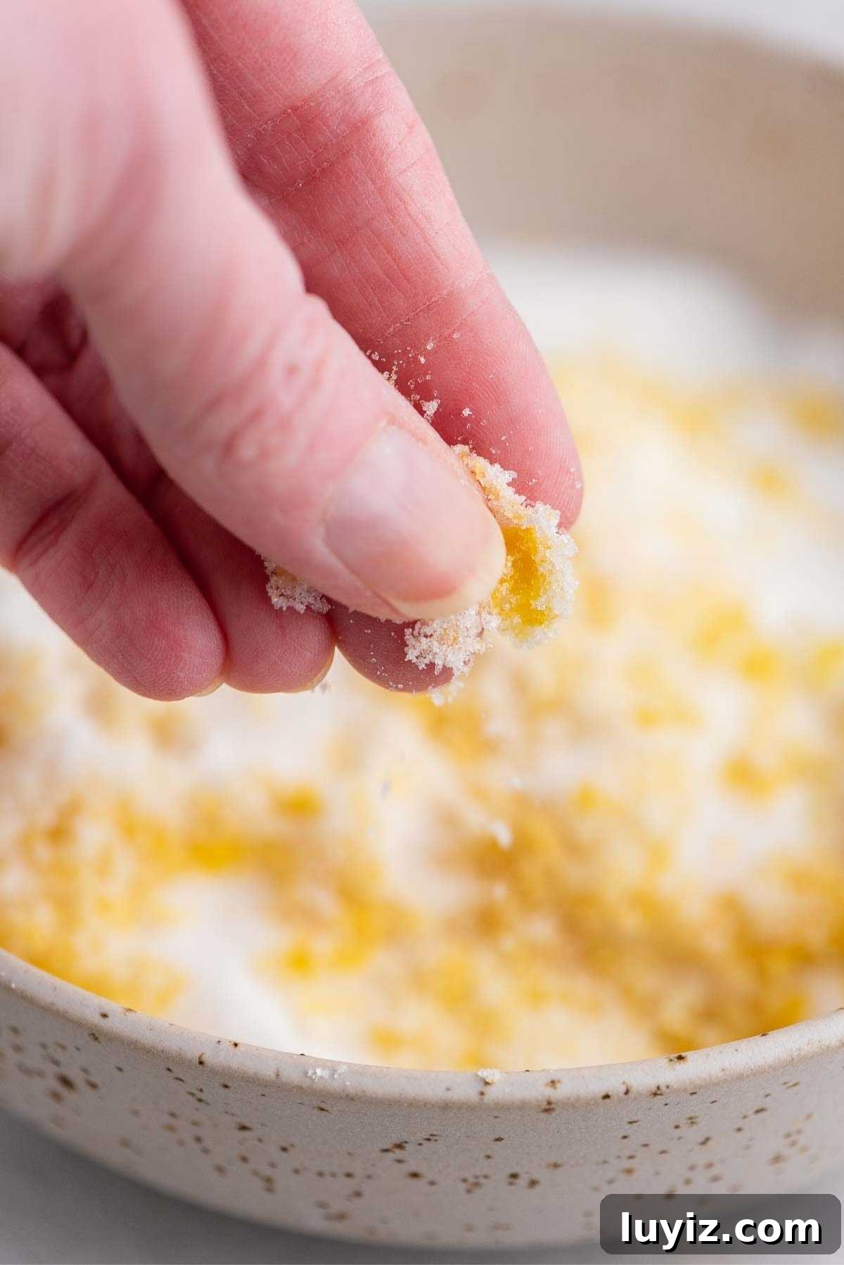 Lemon Poppy Seed Muffins with Zesty Glaze Recipe 5 Rubbing sugar and lemon zest together between pointer finger and thumb over a bowl.