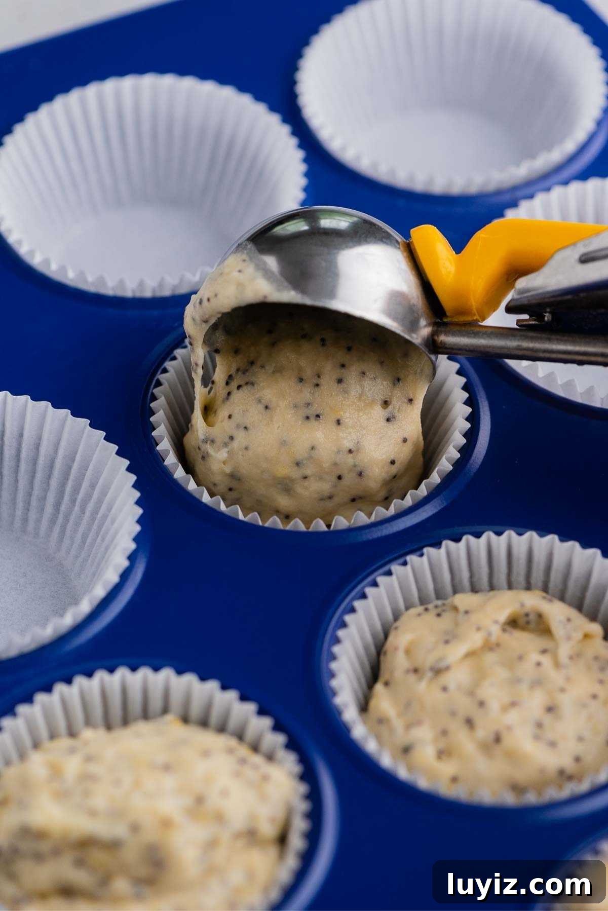 Lemon Poppy Seed Muffins with Zesty Glaze Recipe 9 Adding lemon poppy seed muffin batter to a muffin paper liner using a cookie scoop with yellow handle.