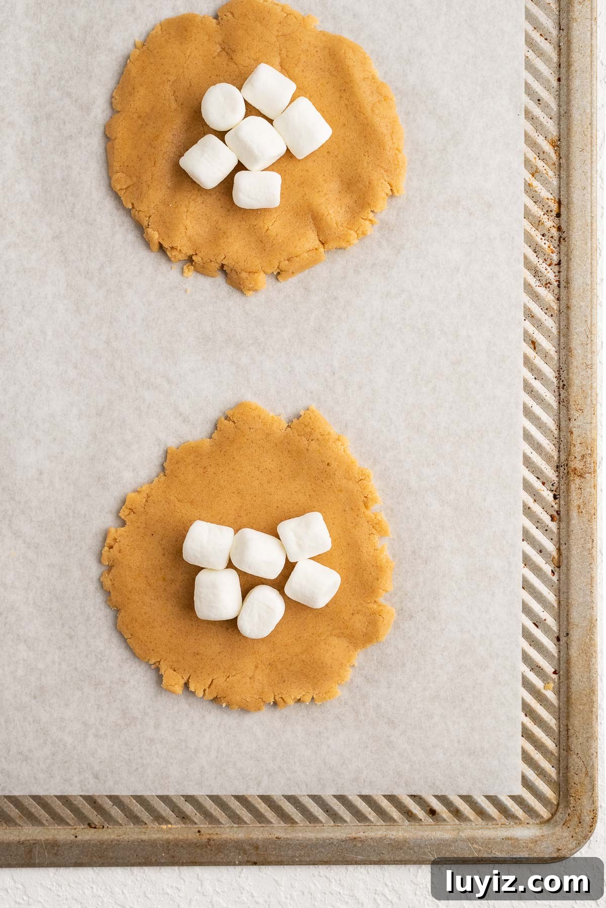 Fluffernutter Sandwich Cookies with Peanut Butter & Marshmallow Filling 8 Six mini marshmallows placed on fluffernutter cookie discs on parchment paper lined baking sheet.