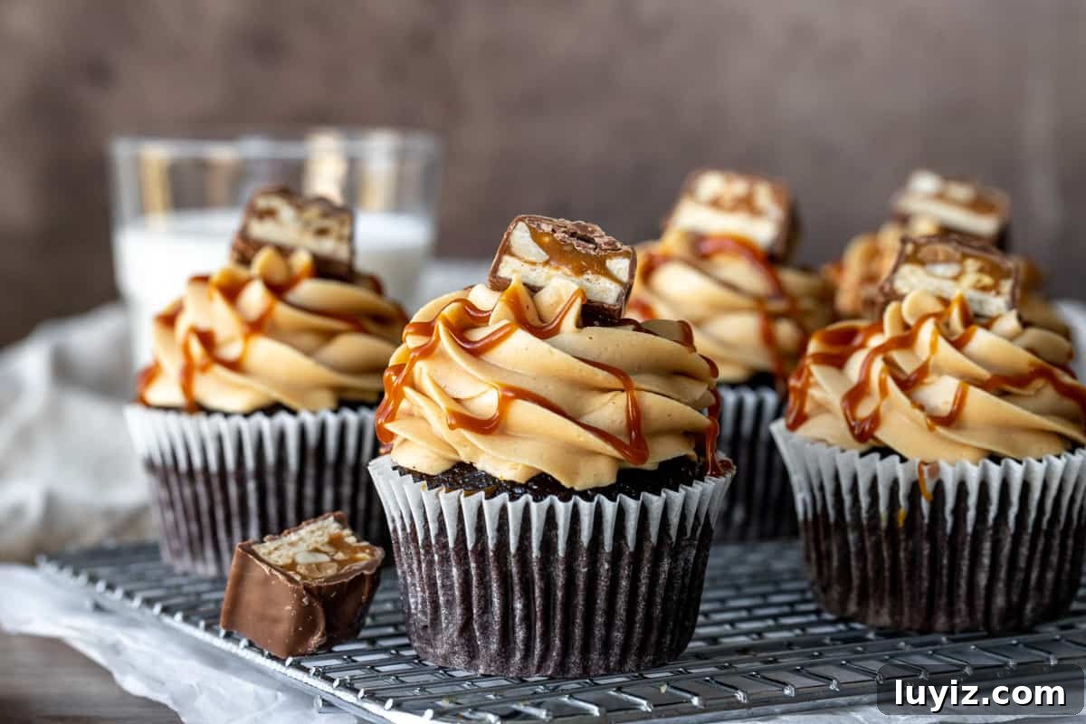Decadent Snickers Cupcakes Recipe with Salted Caramel Drizzle 3 Cooling rack with chocolate cupcakes topped with peanut butter frosting and piece of snickers bar
