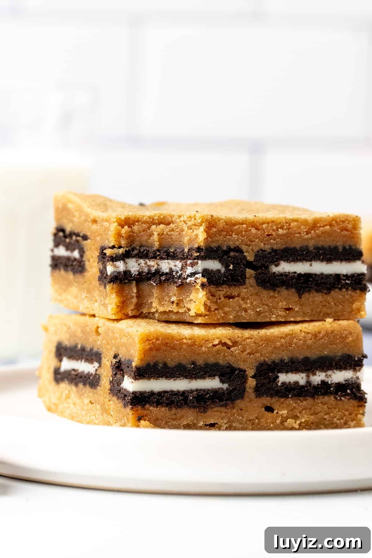 Peanut Butter Oreo Blondies Recipe — Chewy, Chocolate-Stuffed Bars 6 Two peanut butter Oreo blondies, one on top of each other on a plate.
