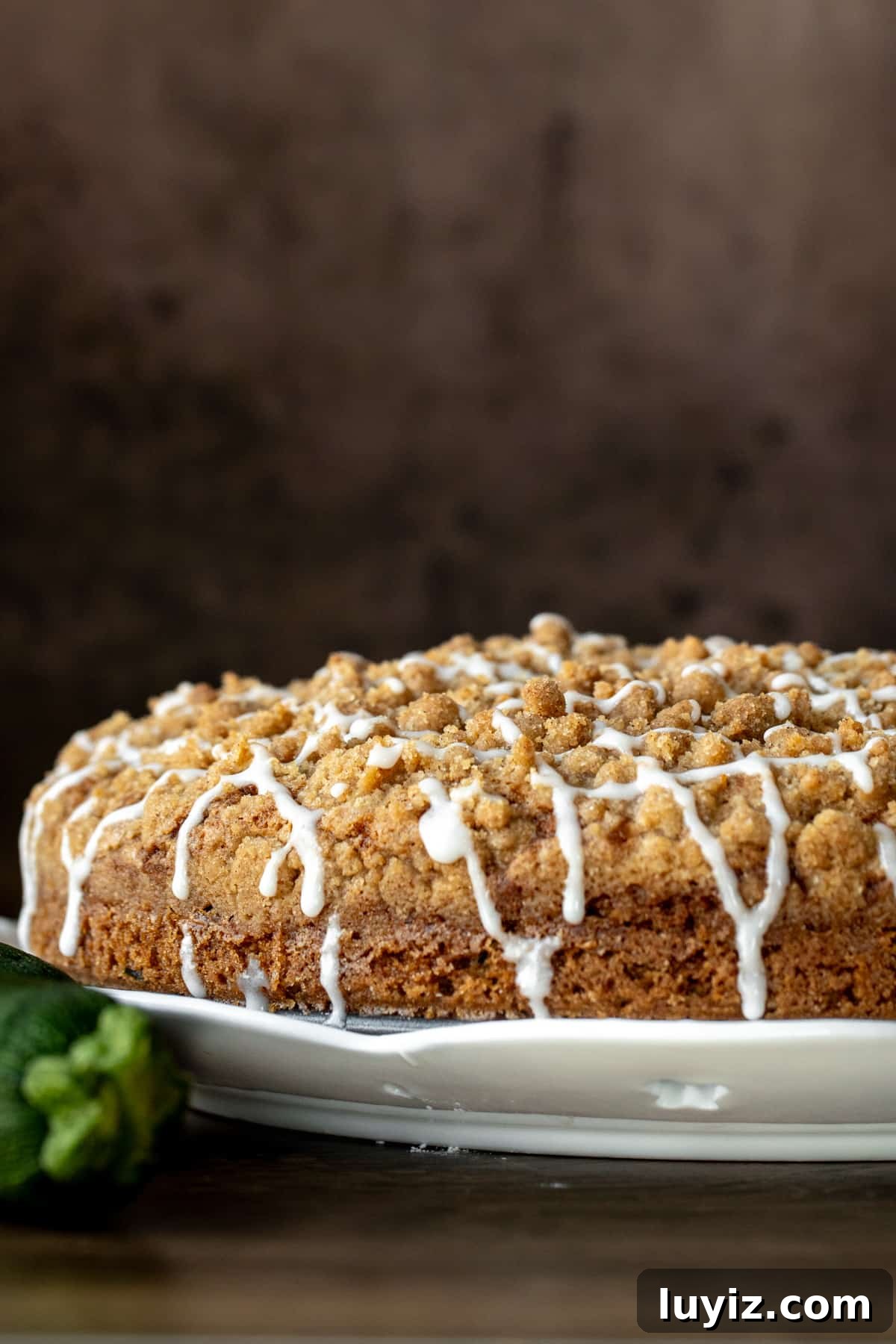 Moist Zucchini Coffee Cake with Cinnamon Streusel 8 9-inch round zucchini coffee cake with a drizzle of glaze on a white plate