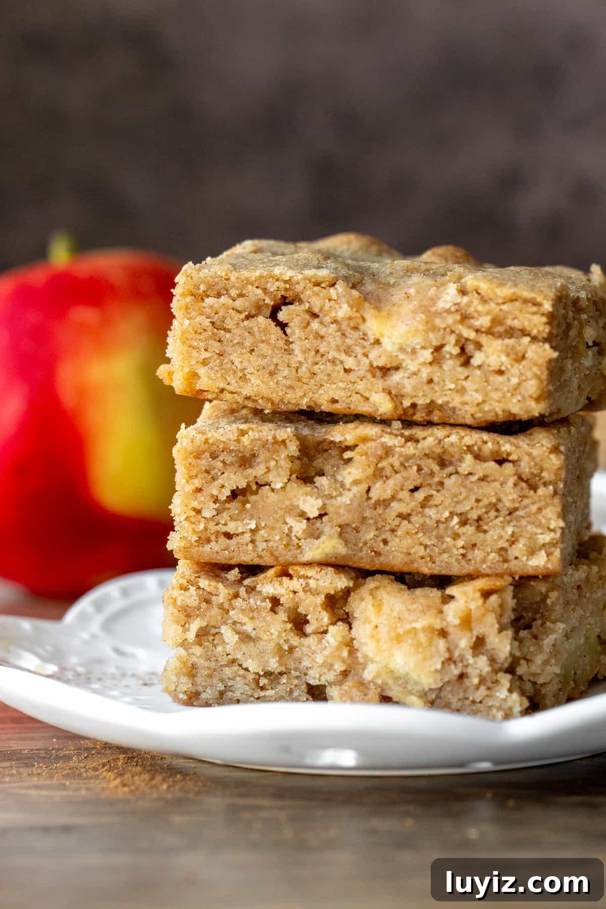 Cinnamon Apple Blondies — Soft, Chewy, Spiced Bite-Sized Treats 7 Three apple cinnamon blondies stacked one on top of the other on a white plate.