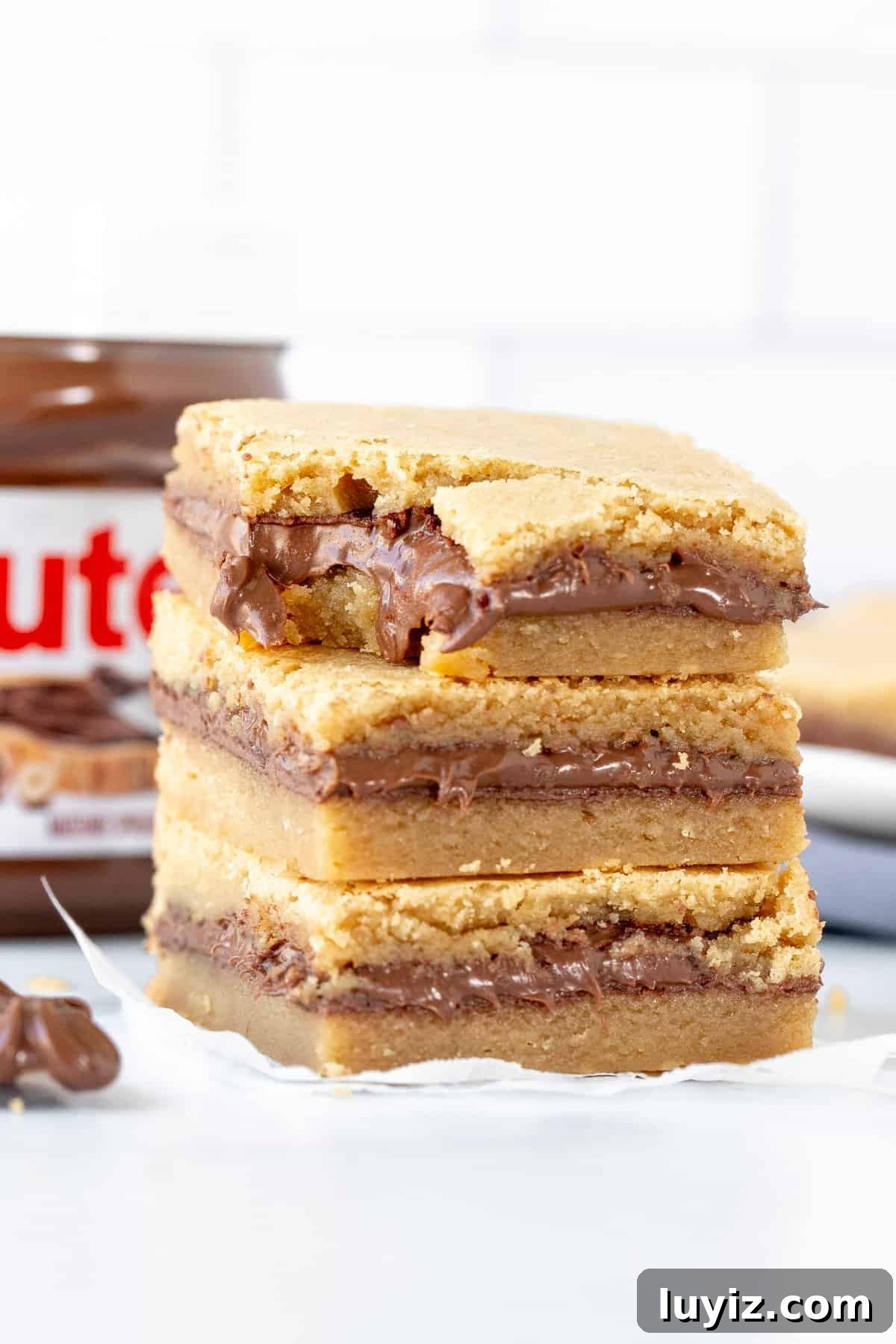 Nutella-Stuffed Blondies: Gooey Chocolate-Hazelnut Bars 9 Stack of three Nutella blondies one on top of each other, with a bit taken out of the top blondie.