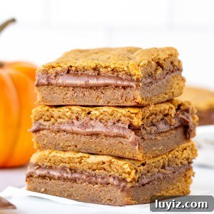 Nutella‑Stuffed Pumpkin Blondies with Gooey Chocolate Center 11 Stack of three pumpkin Nutella blondies with a small pumpkin