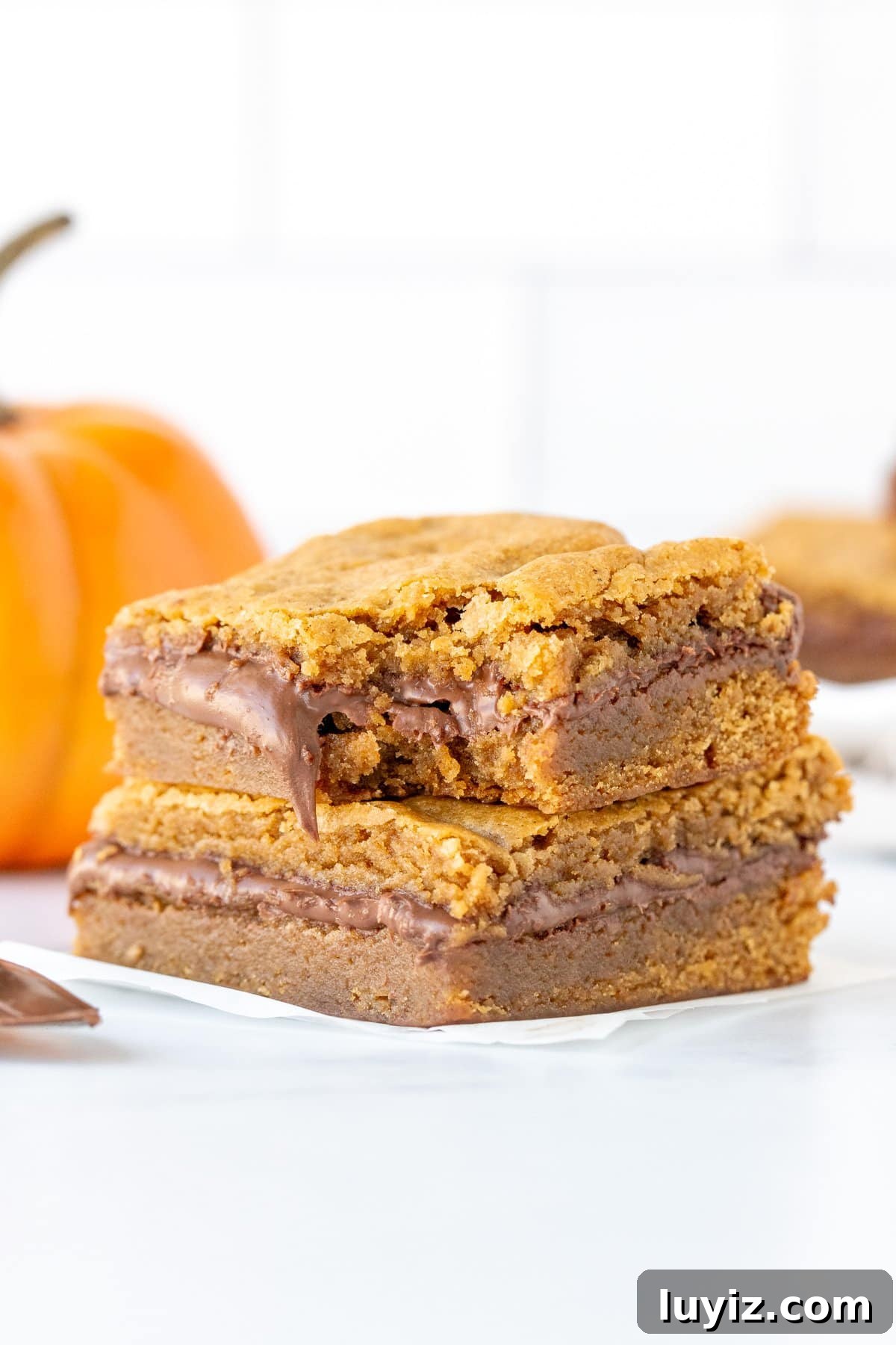 Nutella‑Stuffed Pumpkin Blondies with Gooey Chocolate Center 10 Stack of two Nutella pumpkin blondies, with a bite taken out of the blondie on top