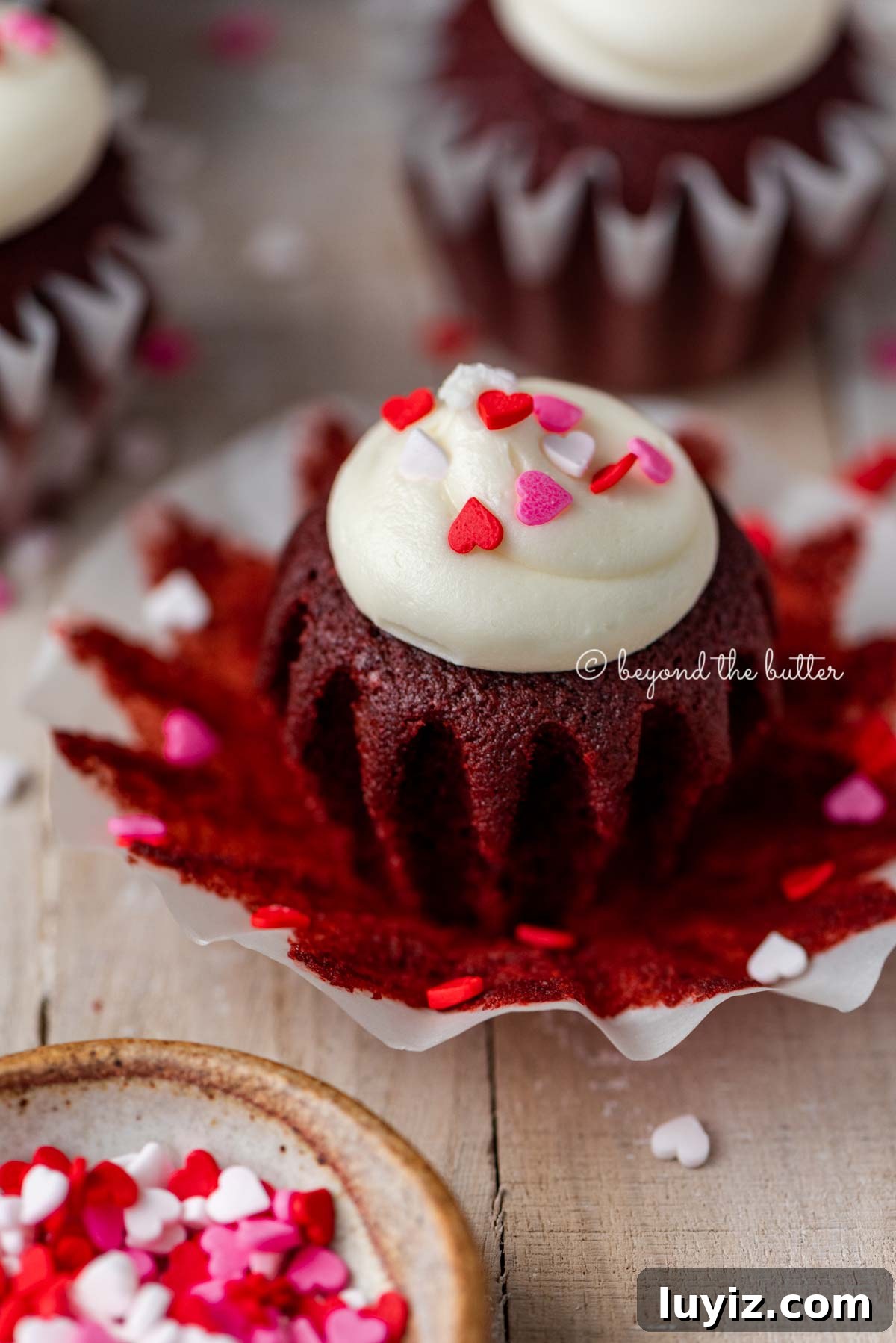Perfect Red Velvet Cupcakes Recipe for Moist, Fluffy Results 2 Opened red velvet cupcake with cream cheese frosting topped with heart sprinkles on a light wood background | All images © Beyond the Butter®