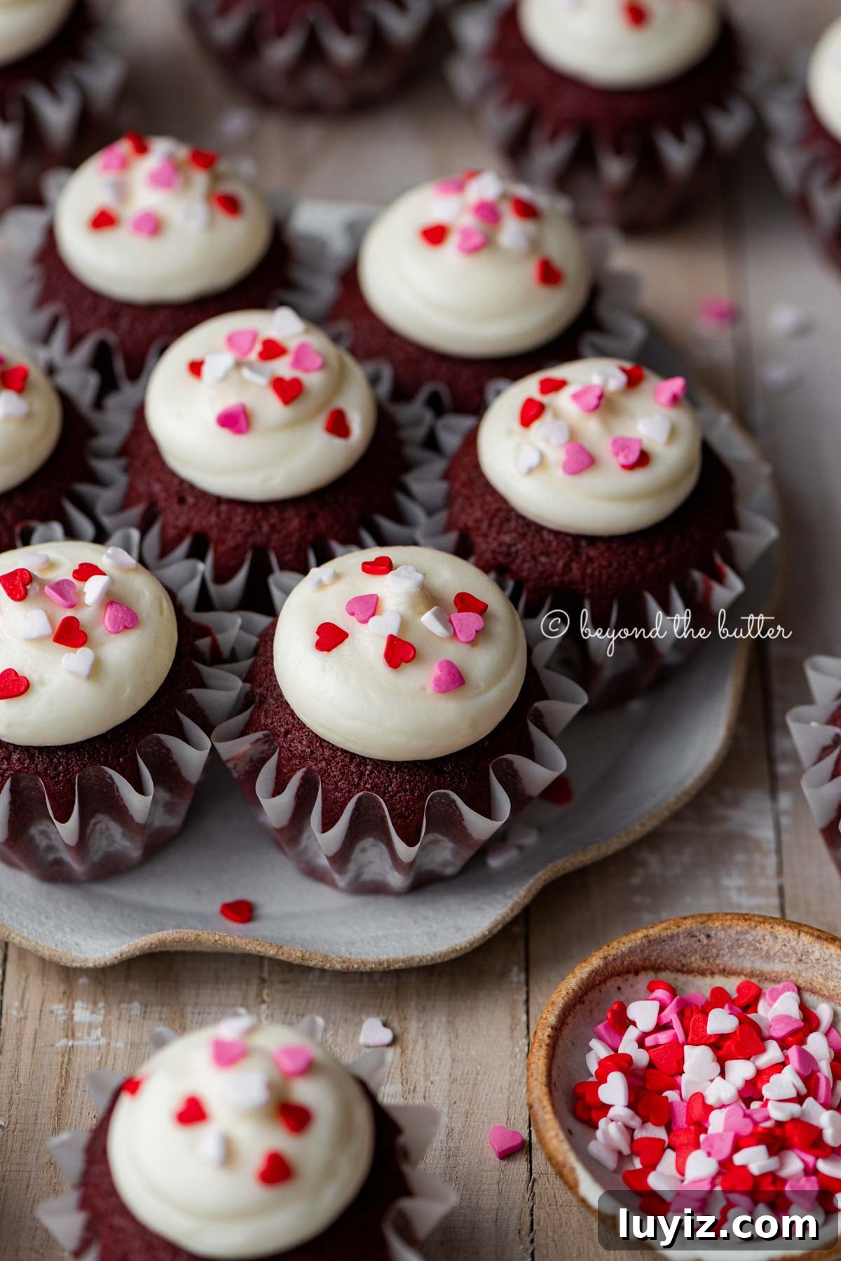 Perfect Red Velvet Cupcakes Recipe for Moist, Fluffy Results 3 Dessert plate with homemade red velvet cupcakes with cream cheese frosting topped with heart sprinkles on a light wood background | All images © Beyond the Butter®