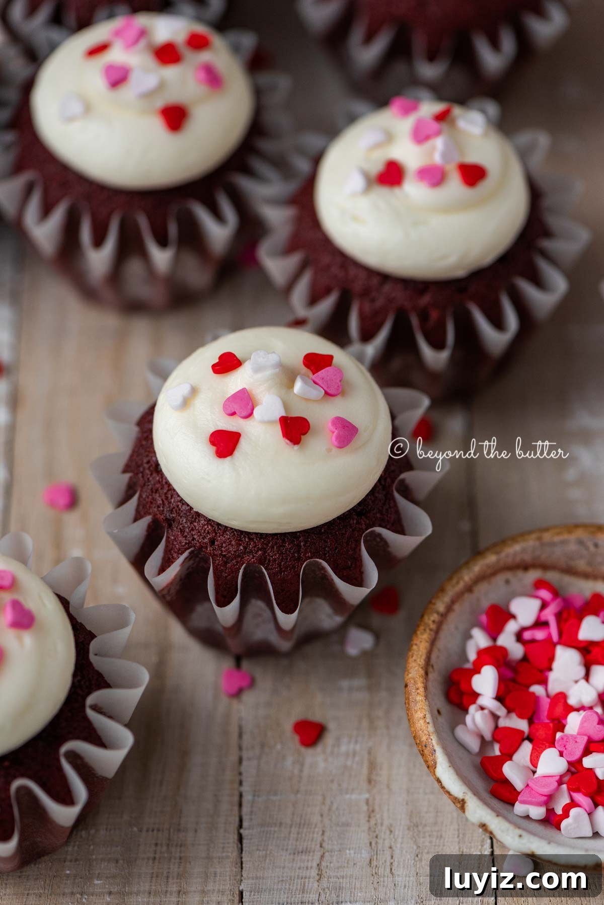 Perfect Red Velvet Cupcakes Recipe for Moist, Fluffy Results 5 Homemade red velvet cupcakes with cream cheese frosting topped with heart sprinkles on a light wood background | All images © Beyond the Butter®