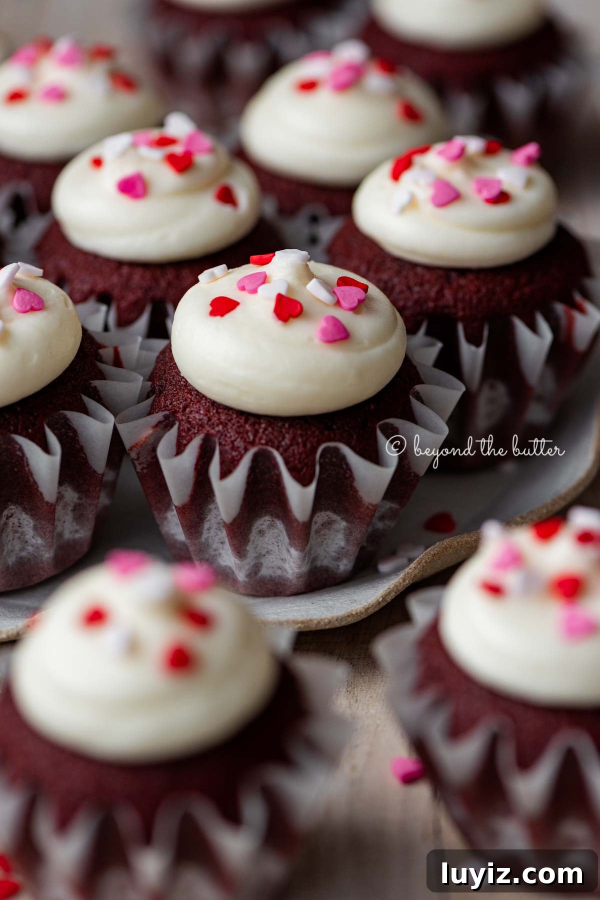 Perfect Red Velvet Cupcakes Recipe for Moist, Fluffy Results 6 Dessert plate with homemade red velvet cupcakes with cream cheese frosting topped with heart sprinkles on a light wood background | All images © Beyond the Butter®