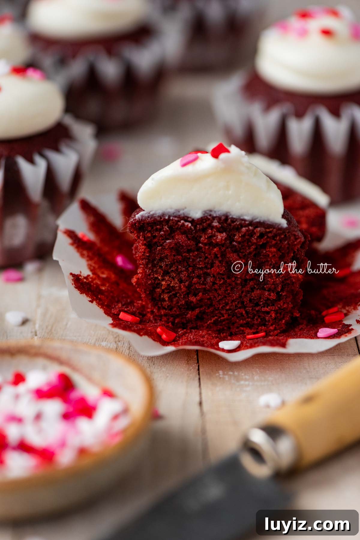 Perfect Red Velvet Cupcakes Recipe for Moist, Fluffy Results 7 Sliced red velvet cupcake with cream cheese frosting topped with heart sprinkles on a light wood background | All images © Beyond the Butter®
