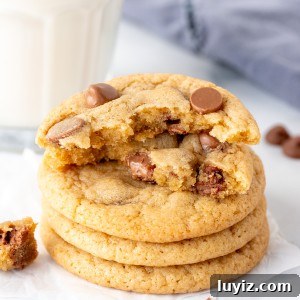 Stack of milk chocolate chip cookies with top cookie broken in half, with glass of milk