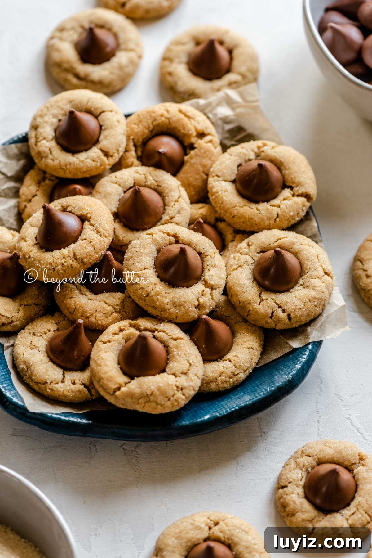 Classic Peanut Butter Blossom Cookies Recipe 7 Angled image of classic peanut butter blossoms on a parchment lined blue dessert platter