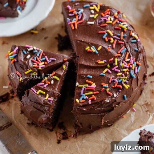 Angled image of sliced single layer chocolate cake on parchment paper with slices of cake on small dessert plates around it and a knife on parchment paper.