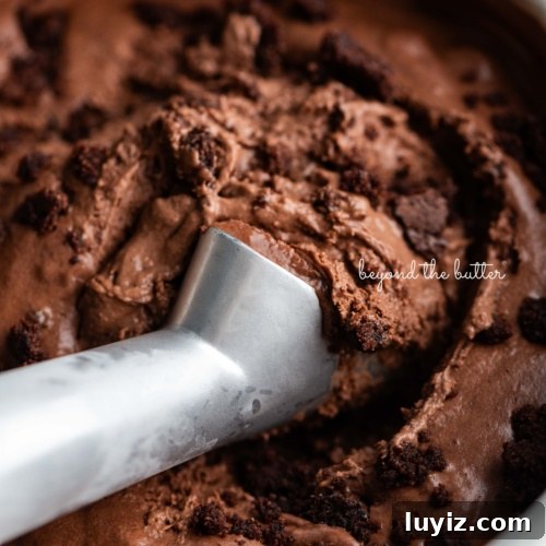 Scooping chocolate brownie ice cream out of a round stainless steel container with a chilled ice cream scoop.