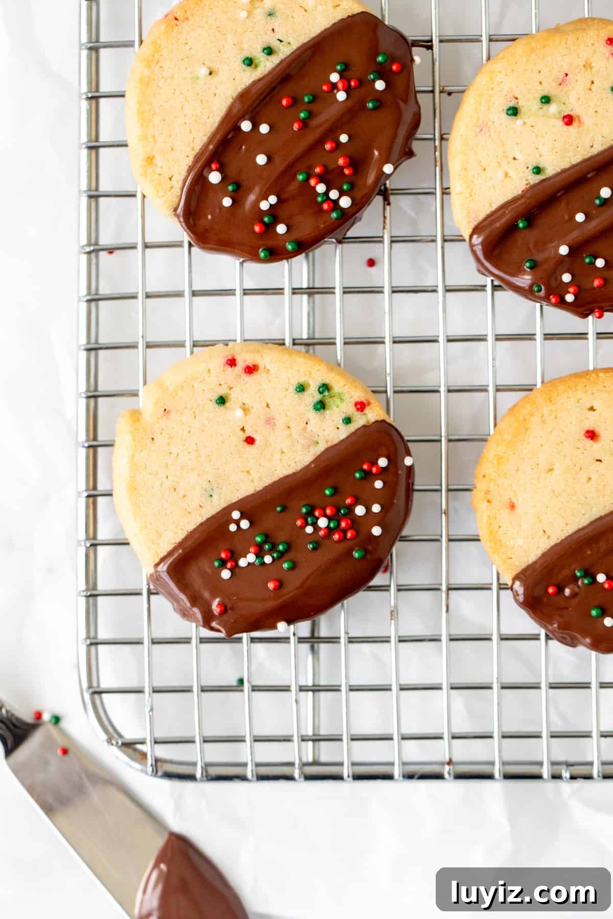 Christmas Sprinkle Slice-and-Bake Cookies: Festive Holiday Recipe 3 Sprinkle slice and bake cookies half dipped in chocolate on a wire rack