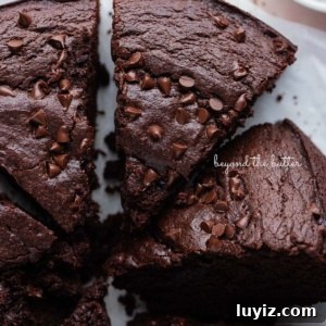 Decadent Chocolate Ricotta Cake Recipe for Moist, Fluffy Results 11 Slices of chocolate ricotta cake topped with chocolate chips on white parchment paper and a small bowl of cocoa powder placed on a light pink tiled background.