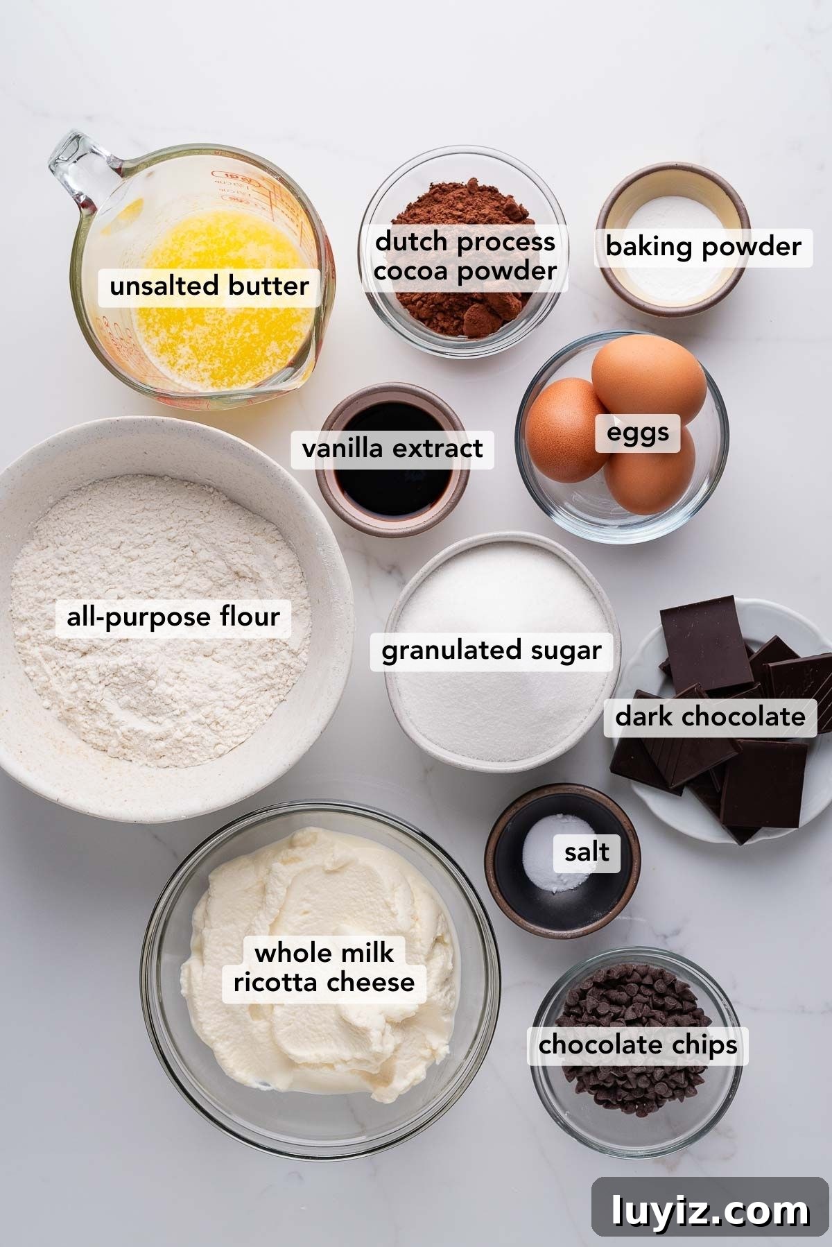 Decadent Chocolate Ricotta Cake Recipe for Moist, Fluffy Results 4 Bowls of different ingredients used to make chocolate ricotta cake on a white marbled background.