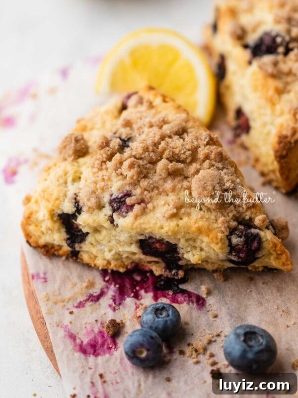 Homemade Donuts from Scratch: Classic Recipe for Soft, Fluffy Donuts 12 Lemon blueberry scones with streusel topping placed on a parchment paper lined round wooden serving plate with lemon wedges and blueberries placed around it.