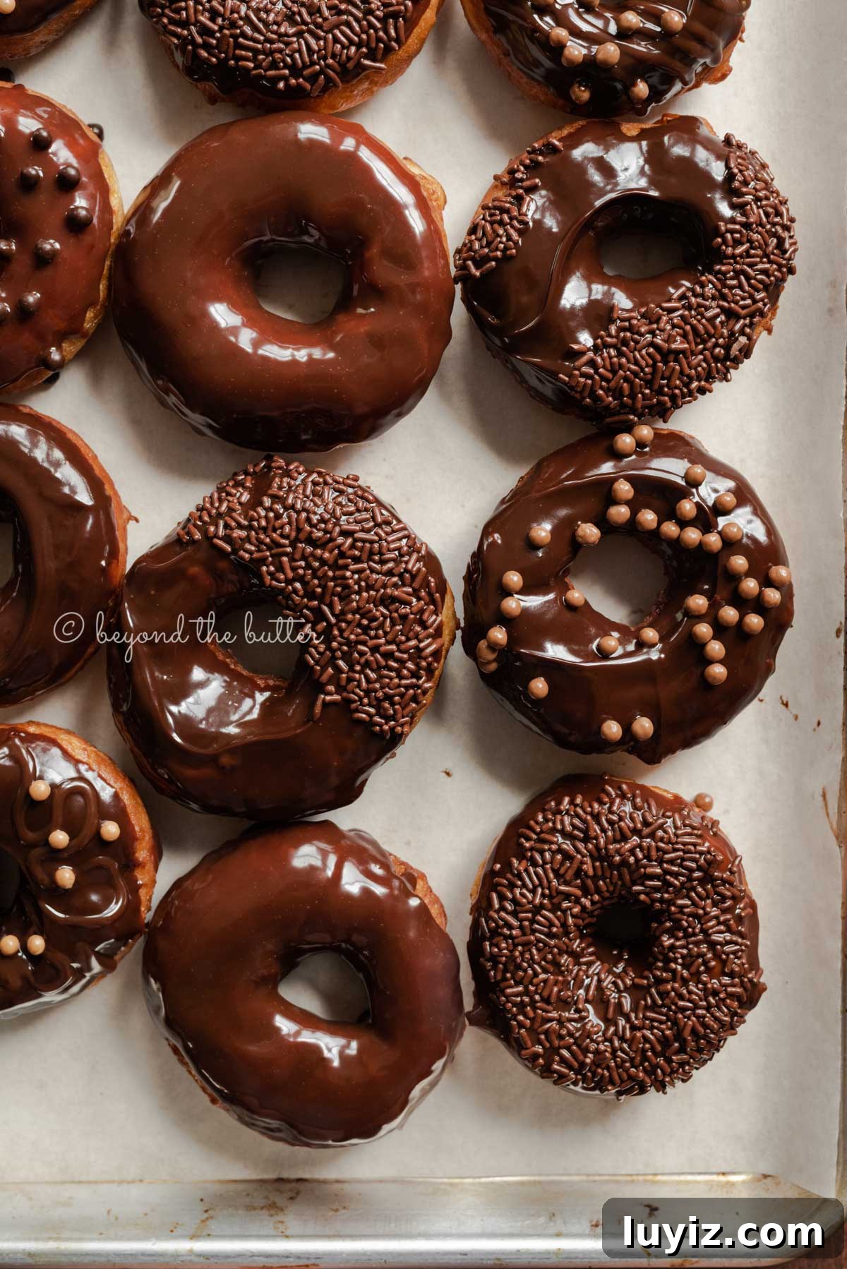 Homemade Donuts from Scratch: Classic Recipe for Soft, Fluffy Donuts 6 Chocolate glazed decorated donuts on a parchment paper lined baking sheet | All Images © Beyond the Butter™