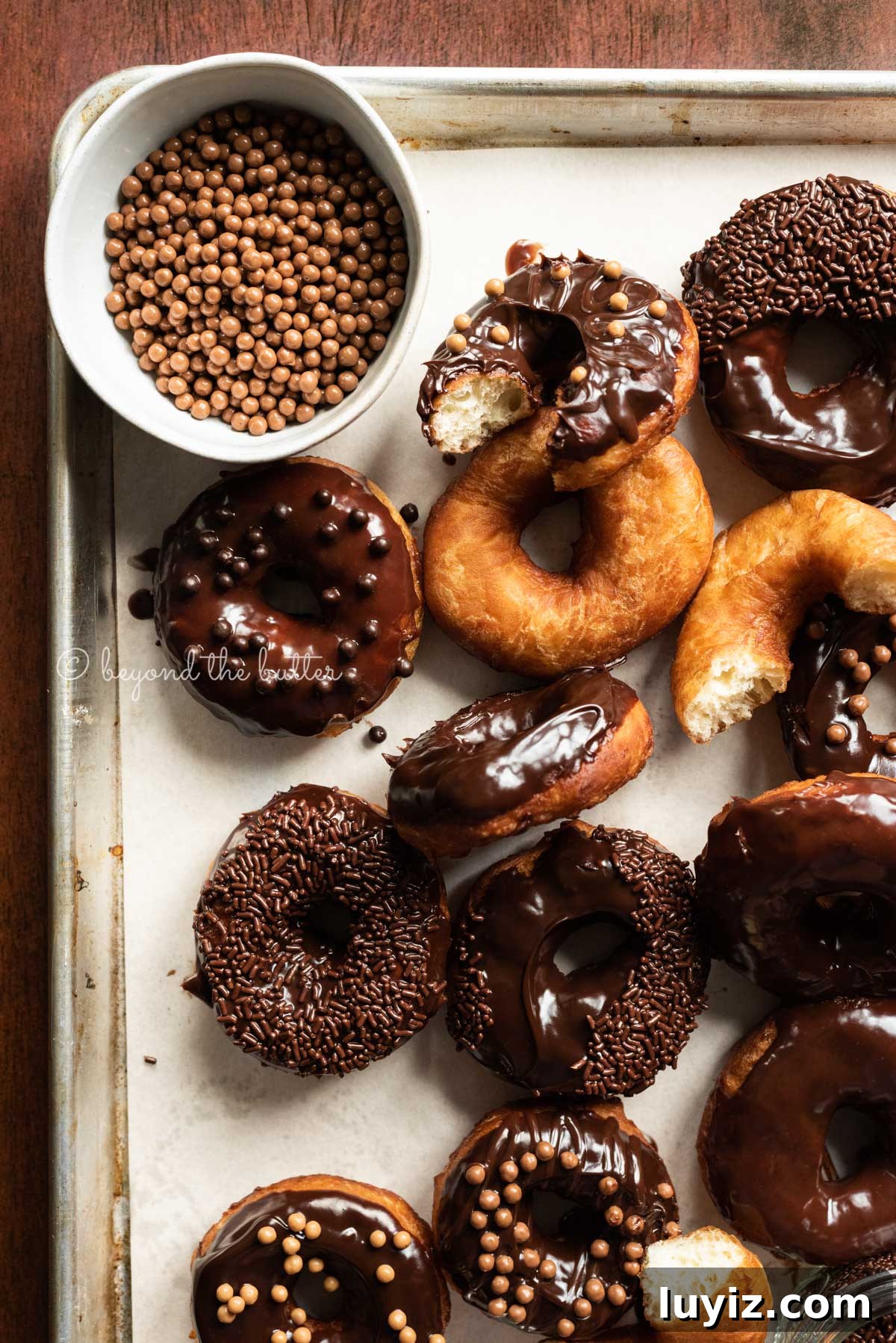 Homemade Donuts from Scratch: Classic Recipe for Soft, Fluffy Donuts 9 Parchment paper lined baking sheet with whole and half eaten donuts with salted caramel pearls in a bowl top left | All Images © Beyond the Butter™