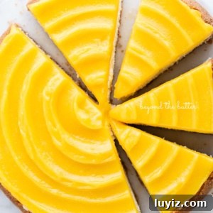 Creamy Lemon Cheesecake Recipe with Zesty Citrus Glaze 18 Lemon cheesecake topped with lemon curd cut into slices on a marble cake plate with white background.