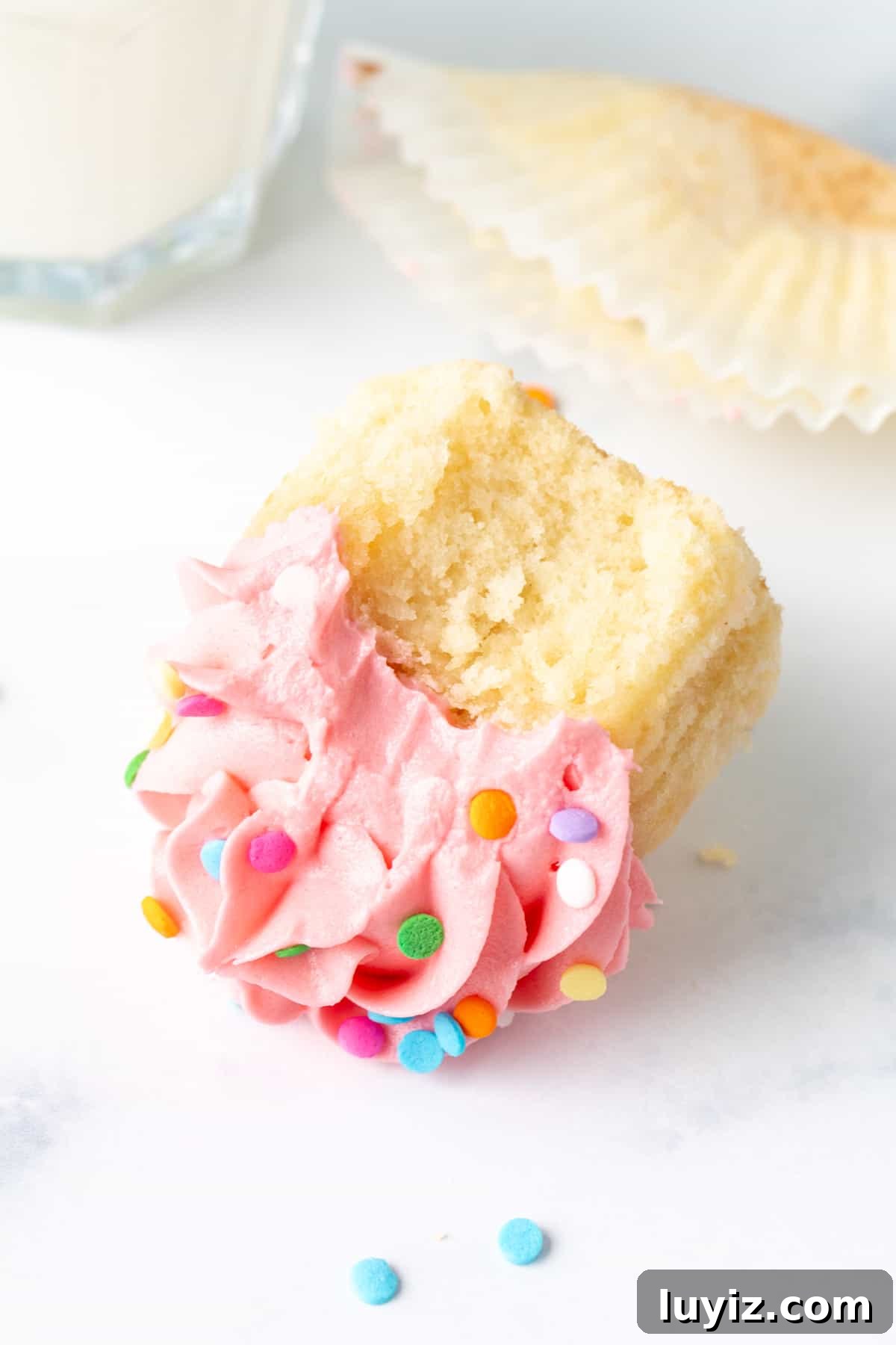 Perfect Vanilla Cupcakes for Two: Simple Small-Batch Recipe 7 Vanilla cupcake with a bite taken out of it, on its side with glass of milk