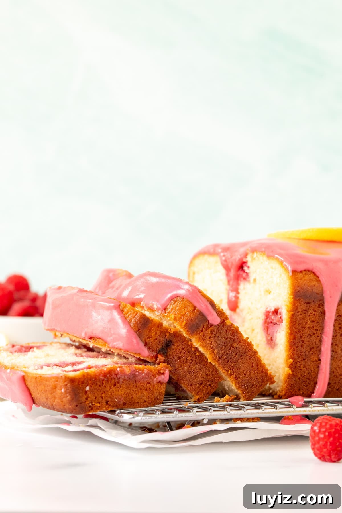 Zesty Lemon Raspberry Quick Bread Recipe 3 Lemon raspberry bread with pink raspberry glaze on a cooling rack with 3 slices cut.