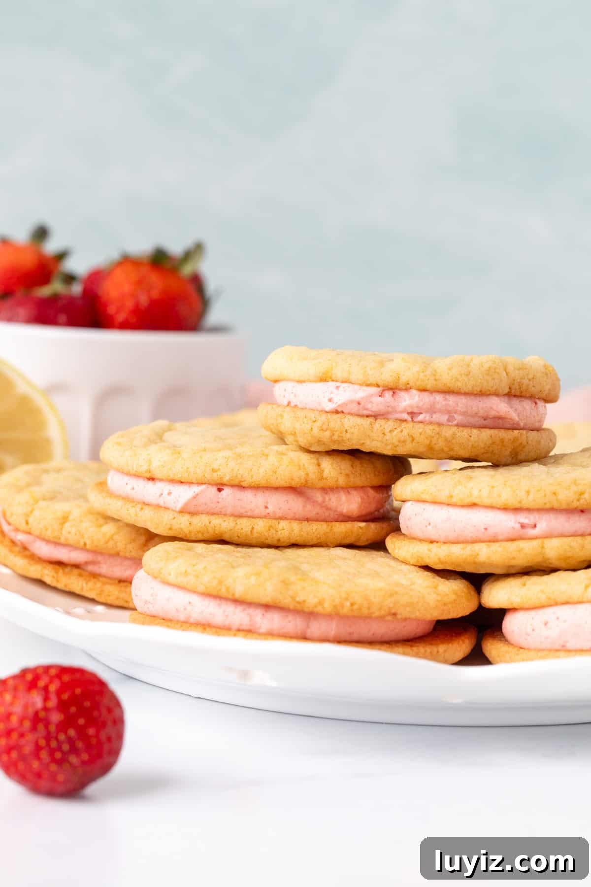 Lemon Sandwich Cookies with Strawberry Buttercream Filling 2 Plate of lemon sandwich cookies with strawberry frosting, with cookies on top of each other