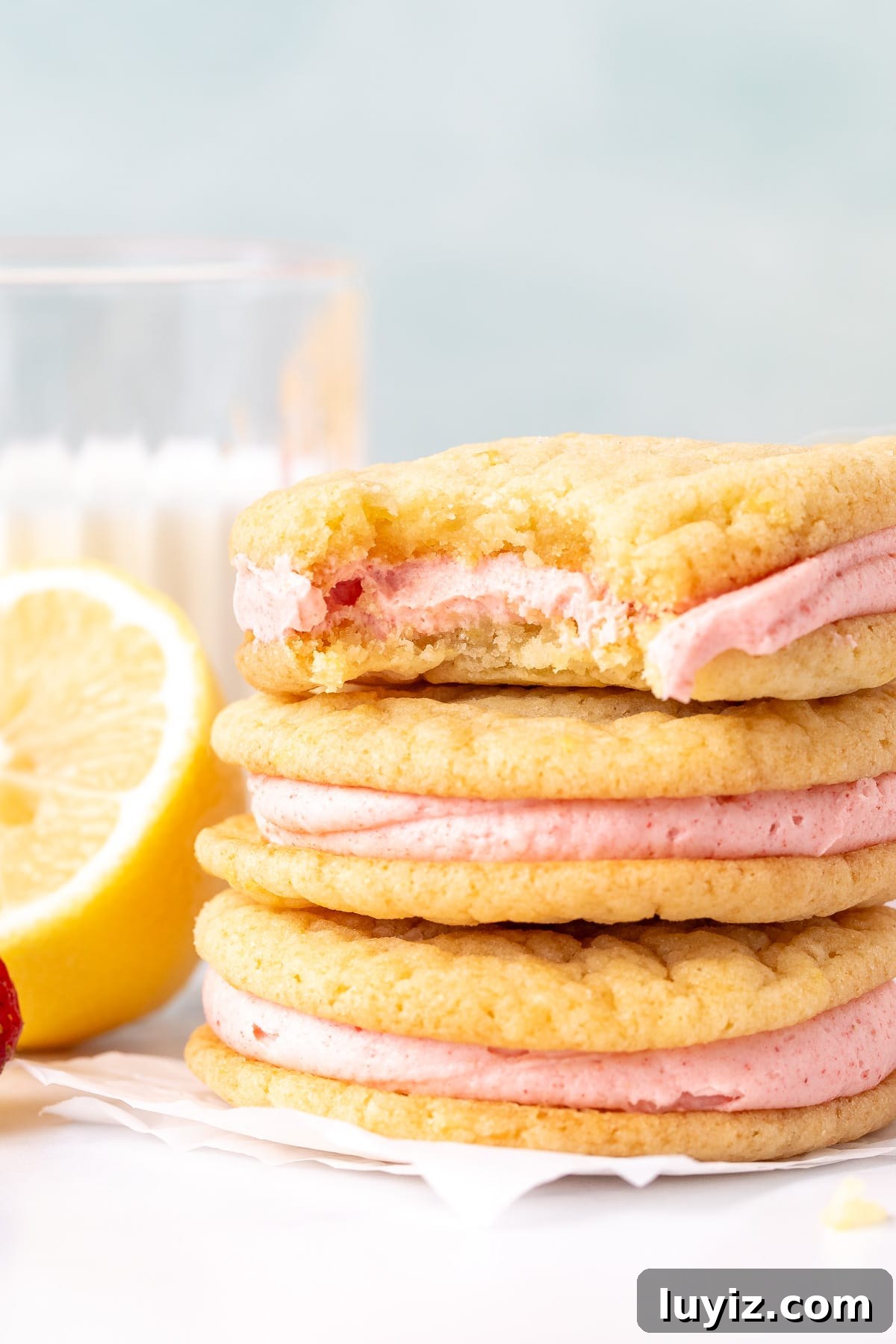 Lemon Sandwich Cookies with Strawberry Buttercream Filling 5 3 lemon sandwich cookies with strawberry frosting in the middle on top of each other, with a bite taken out of the cookie on top