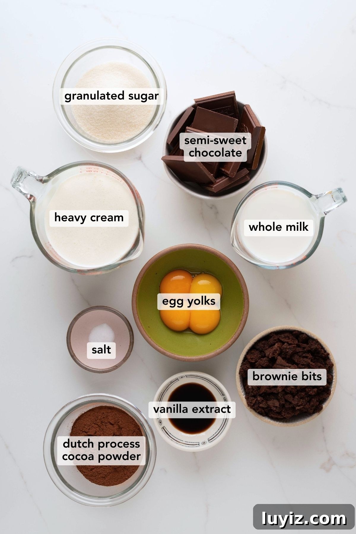 Decadent Chocolate Brownie Ice Cream Recipe & Serving Tips 4 Chocolate brownie ice cream ingredients labeled and placed in separate bowl and measuring cups on a white marbled background.
