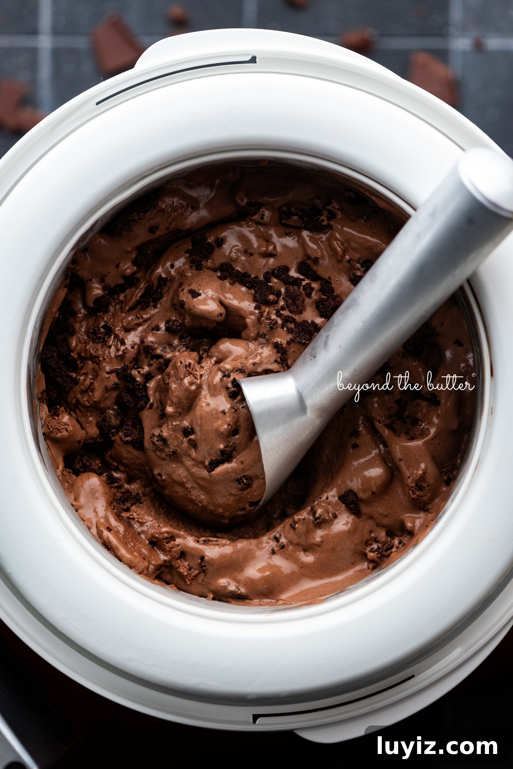 Decadent Chocolate Brownie Ice Cream Recipe & Serving Tips 9 Scooping chocolate brownie ice cream out of the Ankarsrum ice cream maker attachment bowl with a chilled ice cream scoop on a dark background.