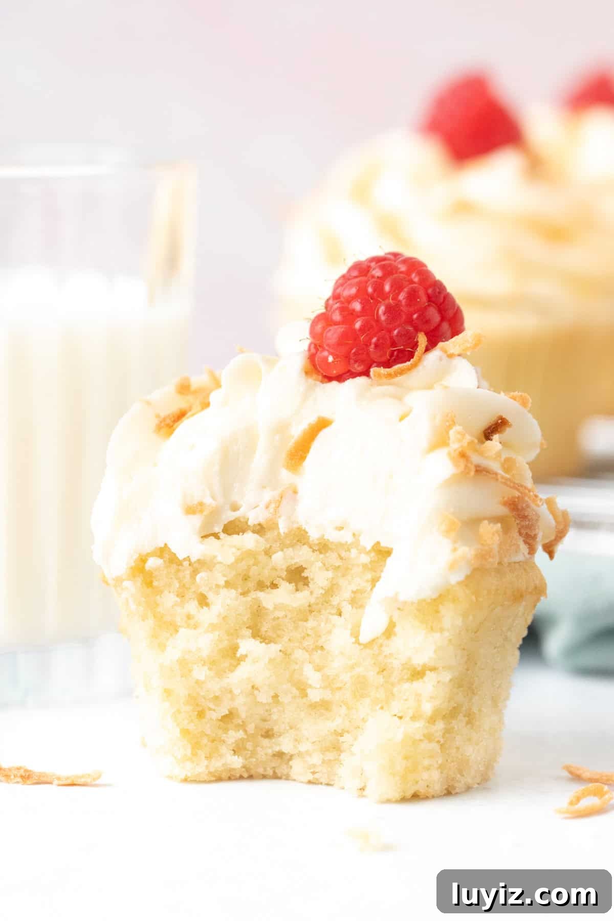 Coconut Cupcakes Recipe: Moist, Tropical Frosted Treats 5 Coconut cupcake with a bite taken out, with glass of milk