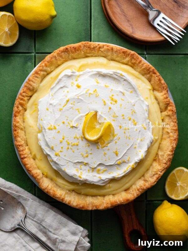 Classic French Bread Recipe for Crispy Crust and Soft Crumb 11 Lemon cream pie topped with fresh whipped cream and lemon zest centered on a green tiled background surrounded by lemons, wood dessert plates, forks, napkin, and pie server.
