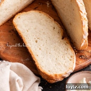 Classic French Bread Recipe for Crispy Crust and Soft Crumb 15 Sliced french bread placed on a round wooden cutting board next to a small pink bowl of butter and a light beige cloth napkin on a black background.