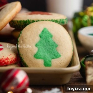 Festive Slice-and-Bake Cookies for Holiday Baking 13 Slice and bake cookies with either a tree, gingerbread man, or candy cane in the center with red or green sparkling sugar edges on a gold baking sheet surrounded by Christmas lights and ornaments on a dark wood background.
