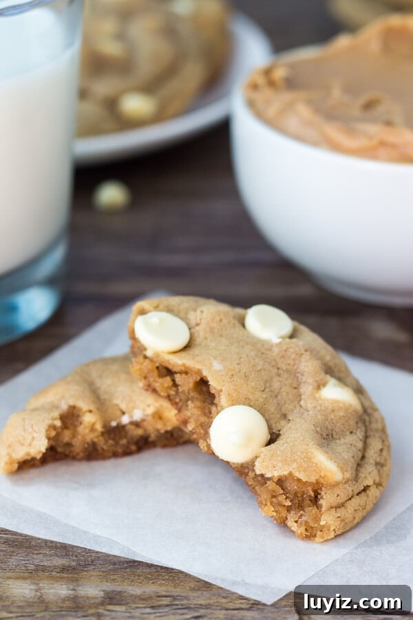 Peanut Butter White Chocolate Chip Cookies Recipe for Chewy Cookies 4 Peanut butter white chocolate chip cookie broken in half. Glass of milk and bowl of peanut butter in the background.