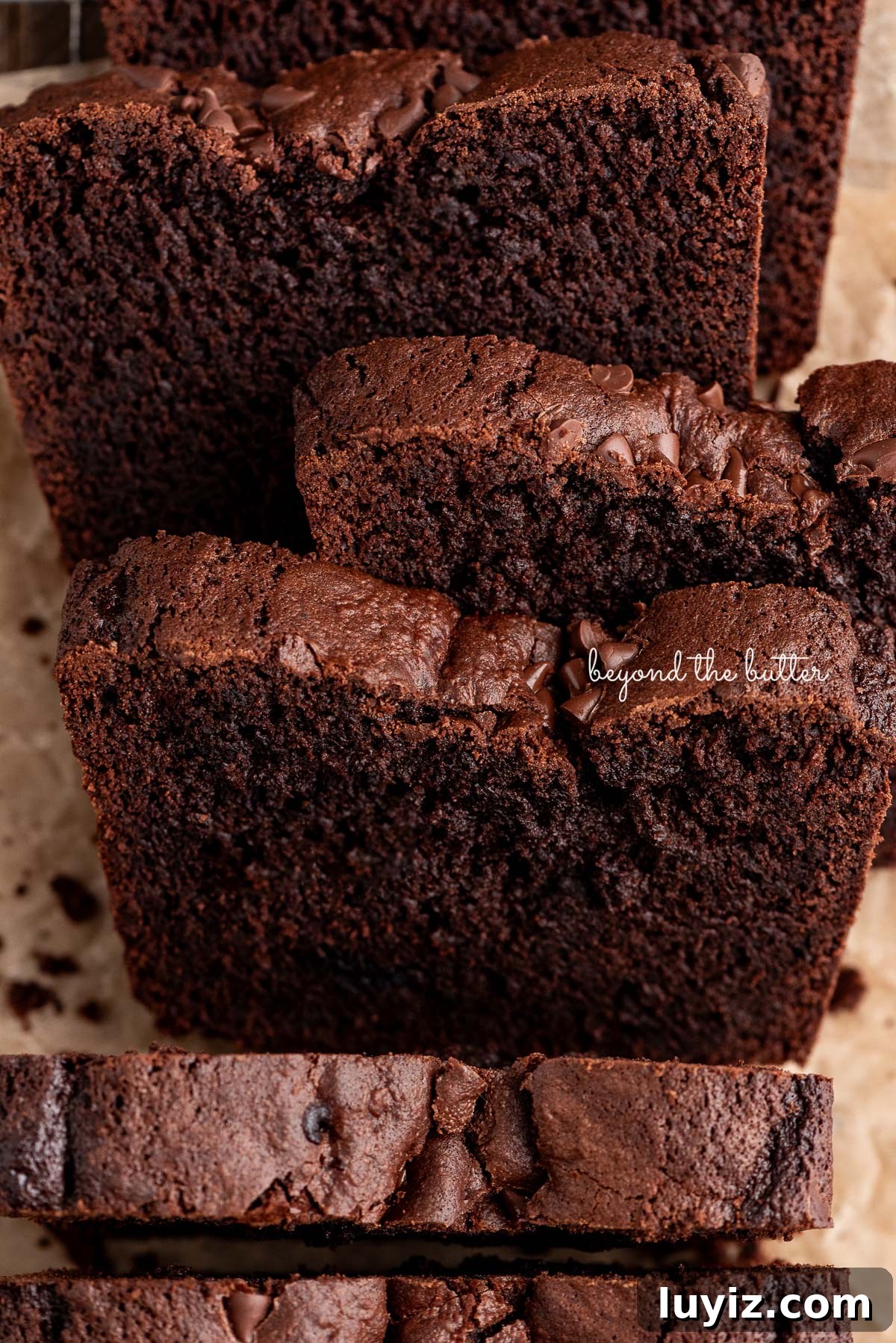Decadent Brownie Loaf Recipe: Fudgy Chocolate Bread Tutorial 2 Slices of dense fudgy brownie bread on a brown parchment paper lined cooling rack on a wood background.