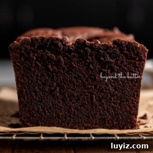 Decadent Brownie Loaf Recipe: Fudgy Chocolate Bread Tutorial 16 Fudgy brownie bread with end cut off on a brown parchment paper lined cooling rack on a dark wood background.