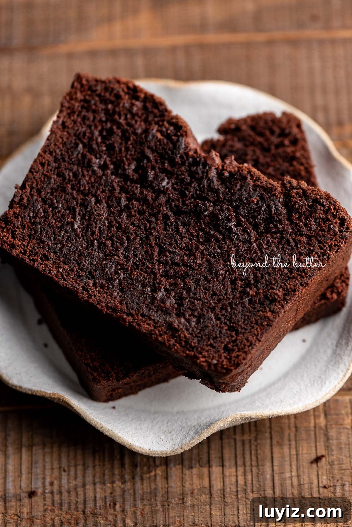 Decadent Brownie Loaf Recipe: Fudgy Chocolate Bread Tutorial 3 Two thick slices of brownie bread on a cream colored, wavy edged ceramic dessert plate on a dark wood background.