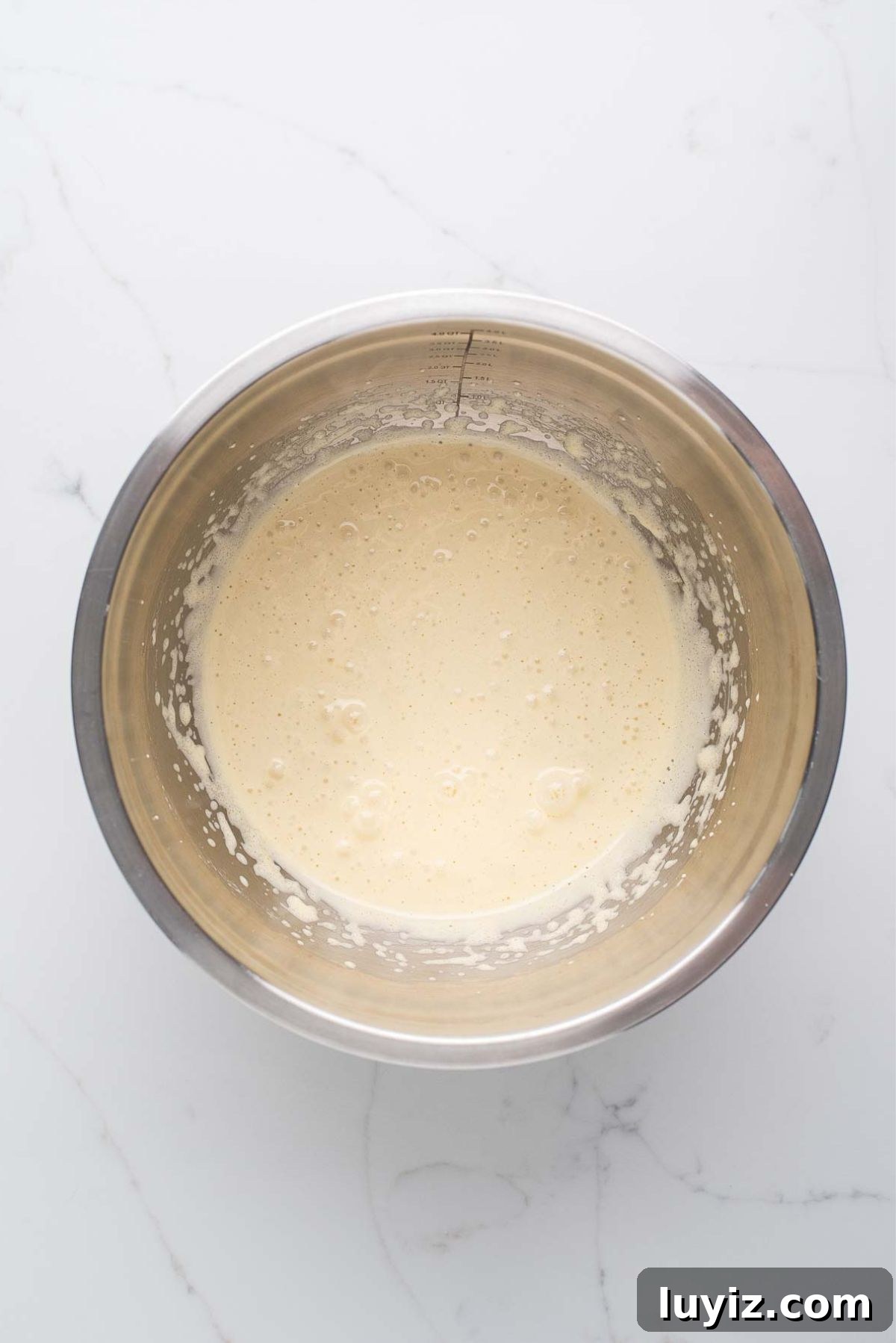 Decadent Brownie Loaf Recipe: Fudgy Chocolate Bread Tutorial 6 Beating eggs and sugar together in a stainless steel mixing bowl on a white marbled background.