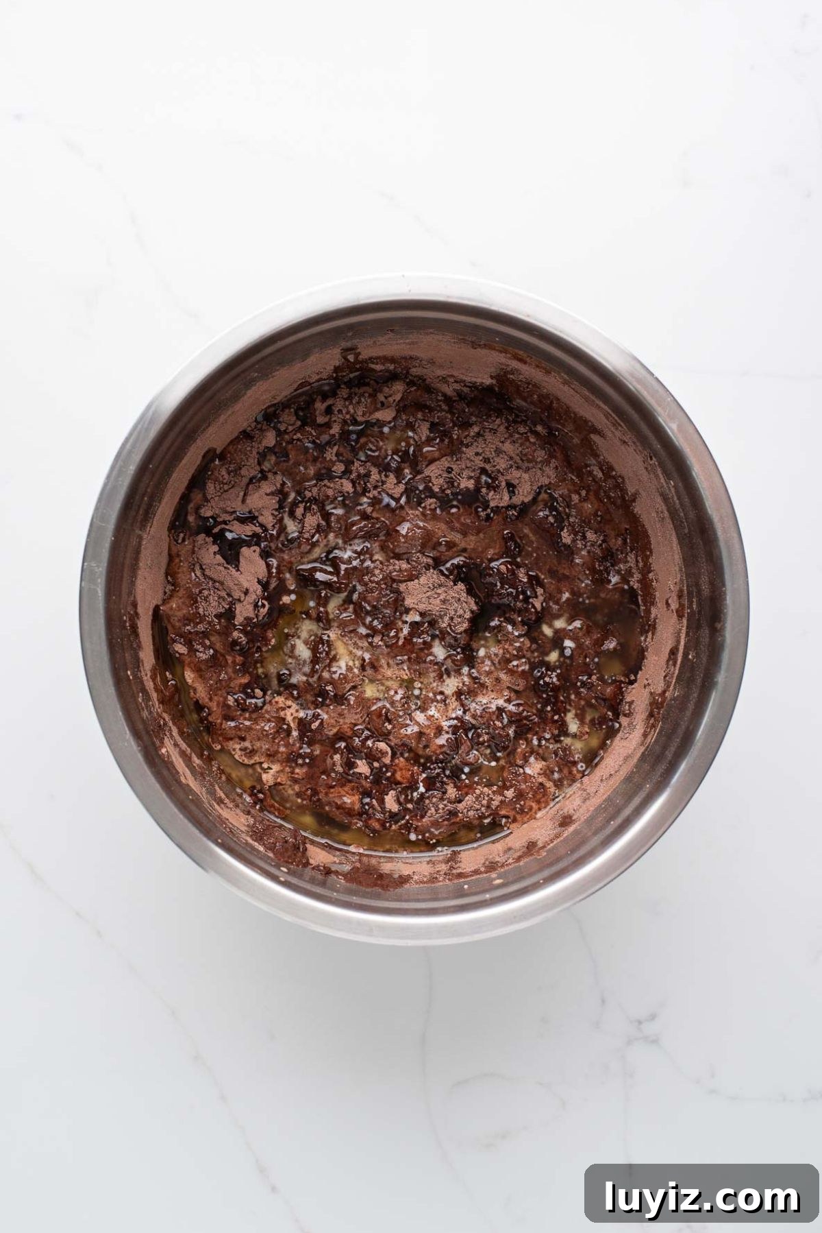 Decadent Brownie Loaf Recipe: Fudgy Chocolate Bread Tutorial 8 Melted butter added to the brownie bread batter in a stainless steel mixing bowl on a white marbled background.