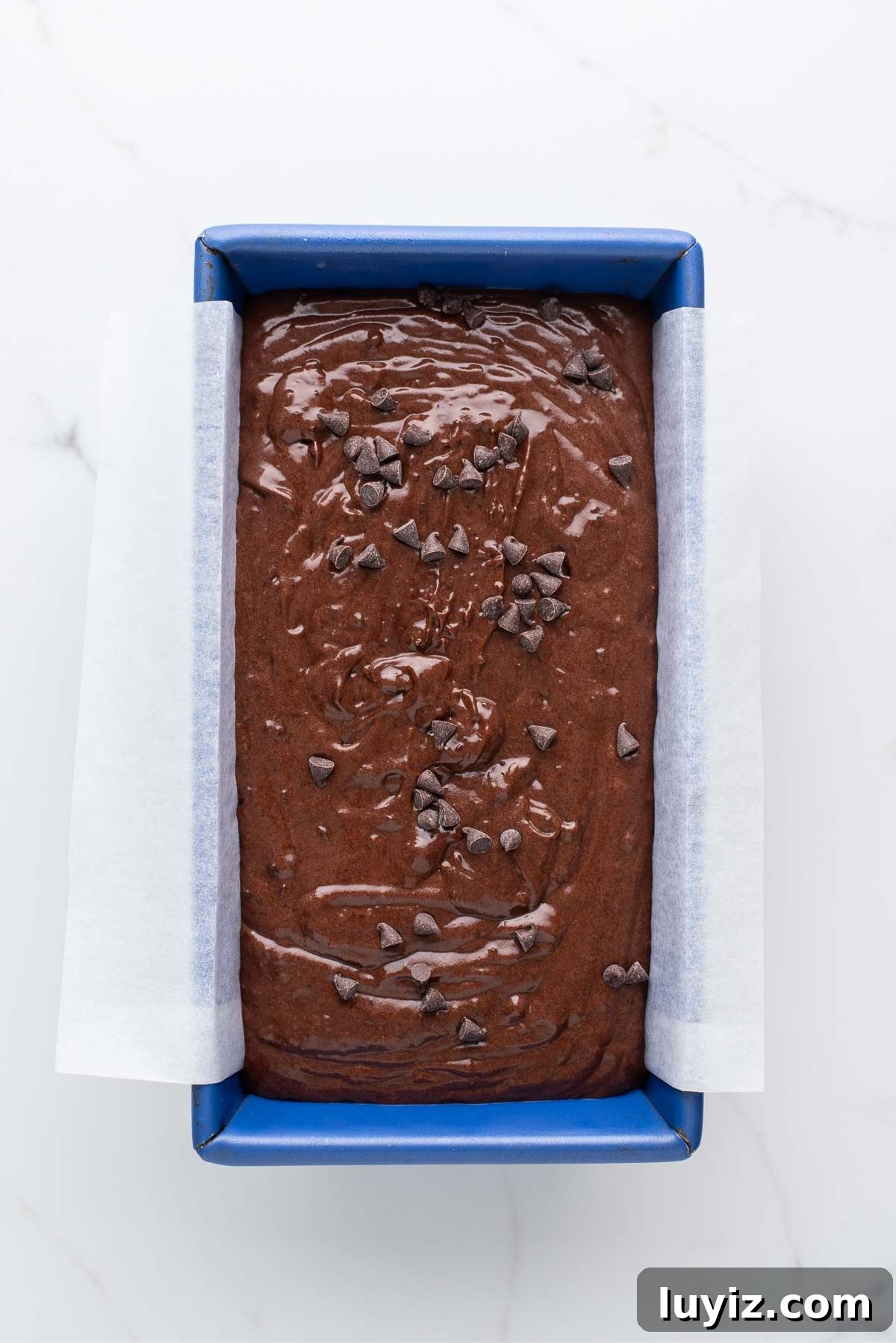 Decadent Brownie Loaf Recipe: Fudgy Chocolate Bread Tutorial 9 Prebaked brownie bread in a blue metal loaf tin on a white marbled background.