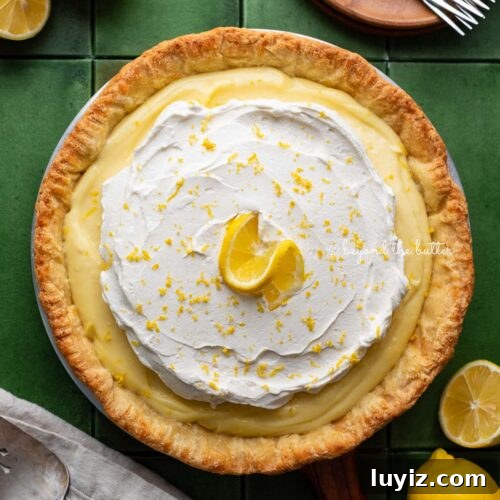 15 Delightful Easter Desserts to Impress Your Guests 12 Lemon cream pie topped with fresh whipped cream and lemon zest centered on a green tiled background surrounded by lemons, wood dessert plates, forks, napkin, and pie server.