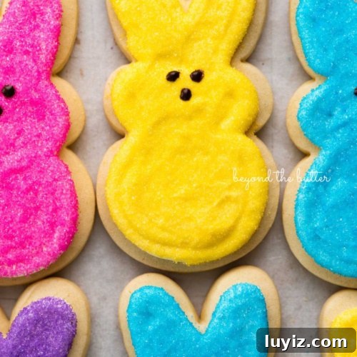 15 Delightful Easter Desserts to Impress Your Guests 3 Easter bunny cut out sugar cookies topped with frosting and colors of pink, yellow, blue, and purple sanding sugars on a parchment paper lined baking sheet.